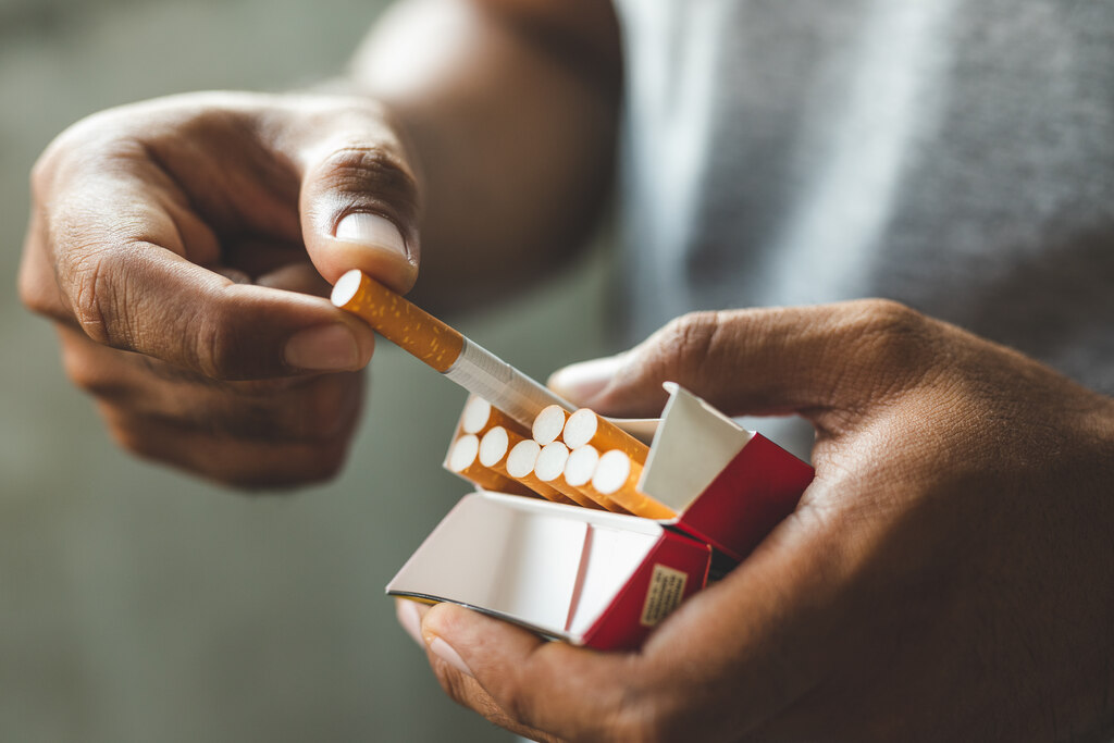 Mãos retirando um cigarro de um maço aberto, ilustrando o hábito do tabagismo e a importância de parar de fumar.