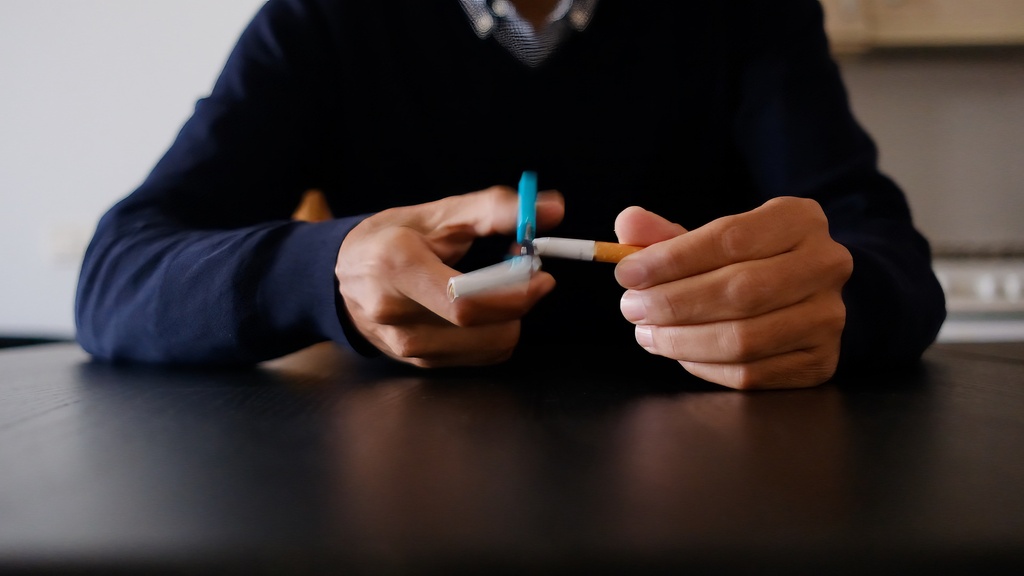 Pessoa segurando um cigarro e cortando ele com uma tesoura, ilustrando a dificuldade de parar de fumar.