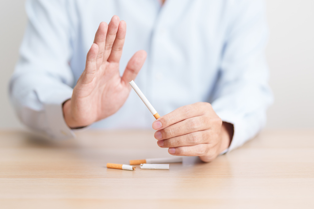 Pessoa fazendo um gesto de recusa enquanto segura um cigarro, com cigarros descartados sobre a mesa.